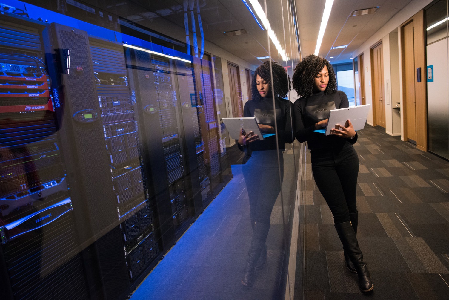 Digital Transformation in Business Featured Image of a Woman Holding a Laptop Next to a Glass Wall With a Server Behind It in a Business Office